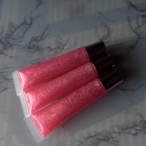 May include: Three pink lip gloss tubes with a shimmery finish. The tubes are clear plastic with a rose gold cap.