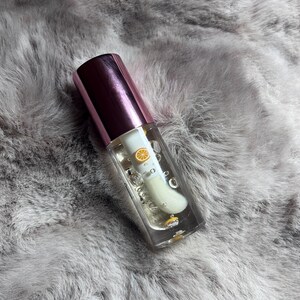 May include: A clear glass bottle with a pink lid containing a clear liquid with a small yellow citrus fruit inside. The bottle is sitting on a gray fuzzy surface.