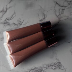 May include: Three tubes of brown lip gloss with clear plastic packaging and gold caps.