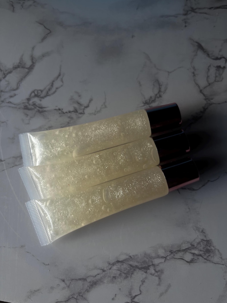 May include: Four clear lip gloss tubes with a shimmery, glittery finish. The tubes have a rose gold cap.