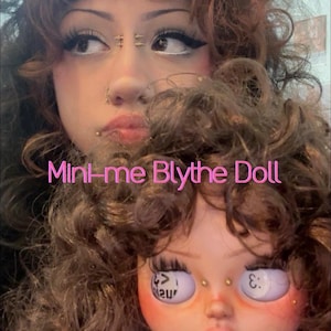 May include: A Blythe doll with curly brown hair, long eyelashes, and facial piercings, featuring light purple eyes with the text < and :3 printed on the irises. The doll wears a white top and has the text Mini-me Blythe Doll overlaid in pink.