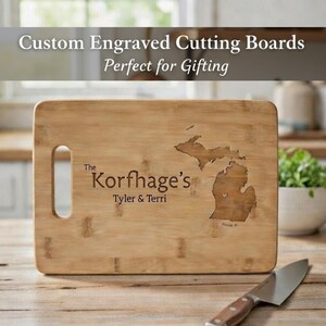 May include: A rectangular bamboo cutting board with a handle, engraved with a state outline and the text "The Korfhage's Tyler & Terri". The text "Custom Engraved Cutting Boards" is at the top.