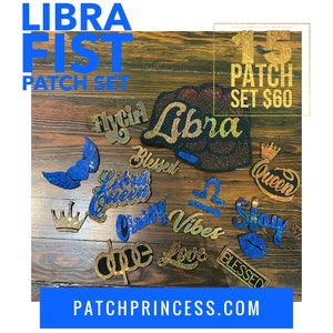 Könnte beinhalten: Eine Sammlung von Strass-Patches mit verschiedenen Designs, darunter das Wort "Libra", ein Schmetterling, eine Krone und die Wörter "Queen", "Blessed" und "Love". Die Patches sind in Blau-, Gold- und Schwarztönen auf einer Holzoberfläche angeordnet. Der Text "LIBRA FIST PATCH SET" befindet sich oben.