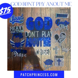 May include: A collection of rhinestone patches in various shapes and sizes, including words like "Blessed", "Brave", and "Chosen". The phrase "GOD DON'T PLAY ABOUT ME" is prominently displayed. The patches are in shades of blue and silver.