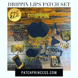 May include: A collection of rhinestone patches on a wooden surface. The patches include the words "DRIPPIN", "Hustle", "GRL PWR", "KEEP IT CUTE", "Boss", and "FASHION". Other patches include lips, a high heel, a bee, and a phone.