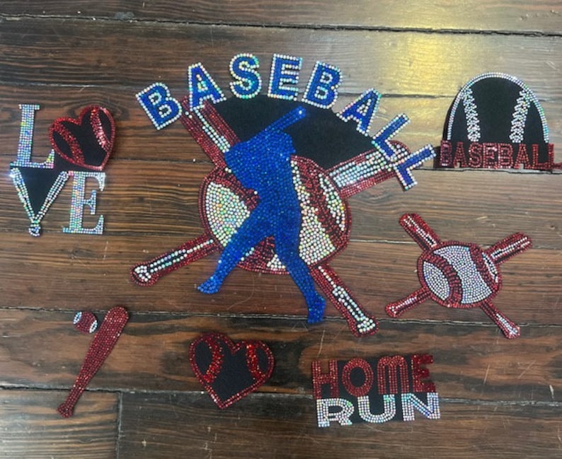 Peut inclure: Une collection d'embellissements en strass sur le th&egrave;me du baseball. L'image comprend le mot "BASEBALL" en strass bleus, un joueur de baseball, une balle, une batte et les mots "LOVE" et "HOME RUN". Les embellissements sont rouges, blancs et bleus.
