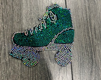 May include: A green and silver rhinestone roller skate applique. The skate has a classic high-top boot design, wheels, and laces. The rhinestones sparkle, creating a dazzling effect. The applique is likely for decorating clothing or accessories.
