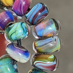 Peut inclure: Un collier de perles de verre colorées avec des motifs tourbillonnants. Les perles sont irisées et présentent une variété de couleurs, notamment le bleu, le vert, le violet et le jaune.