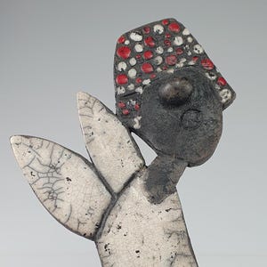 Könnte beinhalten: Eine Keramikskulptur einer Person mit einem rot-weiß gemusterten Hut. Die Skulptur ist aus weißem und schwarzem Ton gefertigt und hat eine strukturierte Oberfläche.