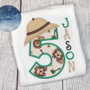 May include: White t-shirt with a green number five, a brown safari hat, and the name "Jason" embroidered on it. The number five is decorated with lions and palm trees.