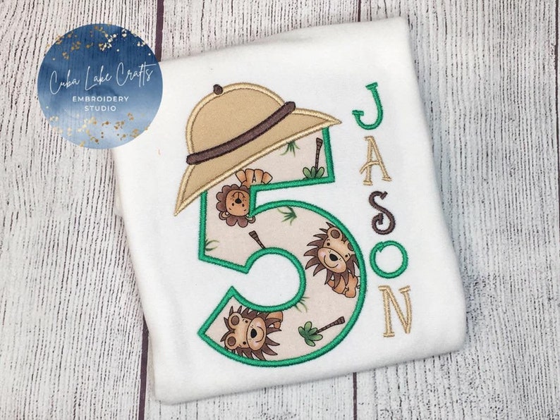 May include: White t-shirt with a green number five, a brown safari hat, and the name "Jason" embroidered on it. The number five is decorated with lions and palm trees.