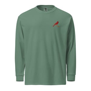 May include: Sage green long-sleeve shirt with a crew neck. A red cardinal bird is embroidered on the left chest, perched on a brown branch. The shirt has a relaxed fit and is made of a soft, comfortable material.
