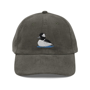 Op de afbeelding: Een groene corduroy baseballpet met een geborduurd beeld van een Bufflehead-eend.