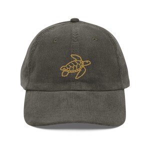 Könnte beinhalten: Eine dunkelgrüne Baseballkappe aus Cord mit einem gestickten gelben Meeresschildkröten-Design.