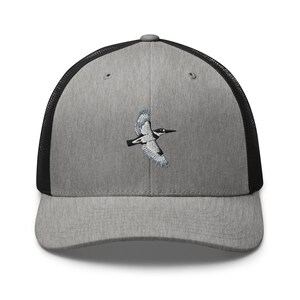 Op de afbeelding: Grijze truckerpet met een zwarte mesh achterkant en een gebogen klep. De pet heeft een geborduurd beeld van een vogel in vlucht, met zwarte, witte en blauwe details. Een casual accessoire.