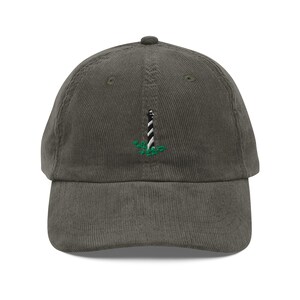 May include: A green corduroy baseball cap with a white and black lighthouse embroidered on the front.