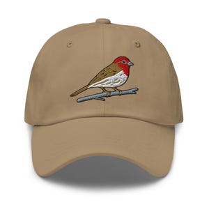 Könnte beinhalten: Beige Baseballkappe mit einem gestickten Vogelmotiv. Der Vogel hat einen roten Kopf, einen braunen Rücken und eine weiße Brust, der auf einem grauen Ast sitzt. Die Kappe hat einen gebogenen Schirm und einen Knopf oben.