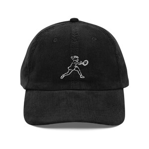 Può includere: Un cappello da baseball in velluto a coste nero con un disegno ricamato bianco di una persona che gioca a tennis.