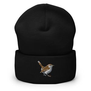 Op de afbeelding: Zwarte gebreide beanie met een geborduurde bruine en witte winterkoning op de voorkant.
