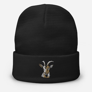 Puede incluir: Gorro negro con una cabeza de cabra bordada en marrón y blanco en la parte delantera.