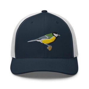 Puede incluir: Gorra de camionero azul marino con parte trasera de malla blanca. El panel frontal presenta un pájaro bordado con detalles amarillos, verdes, grises y negros. La gorra tiene una visera curva y cierre a presión.