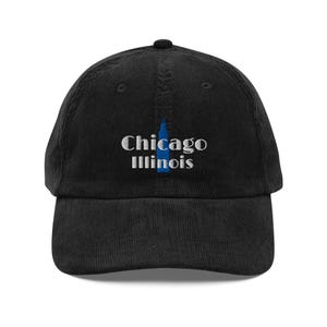 May include: Black corduroy baseball cap with the text "Chicago Illinois" embroidered in white, with a blue skyscraper graphic. The cap has a curved brim and a top button.