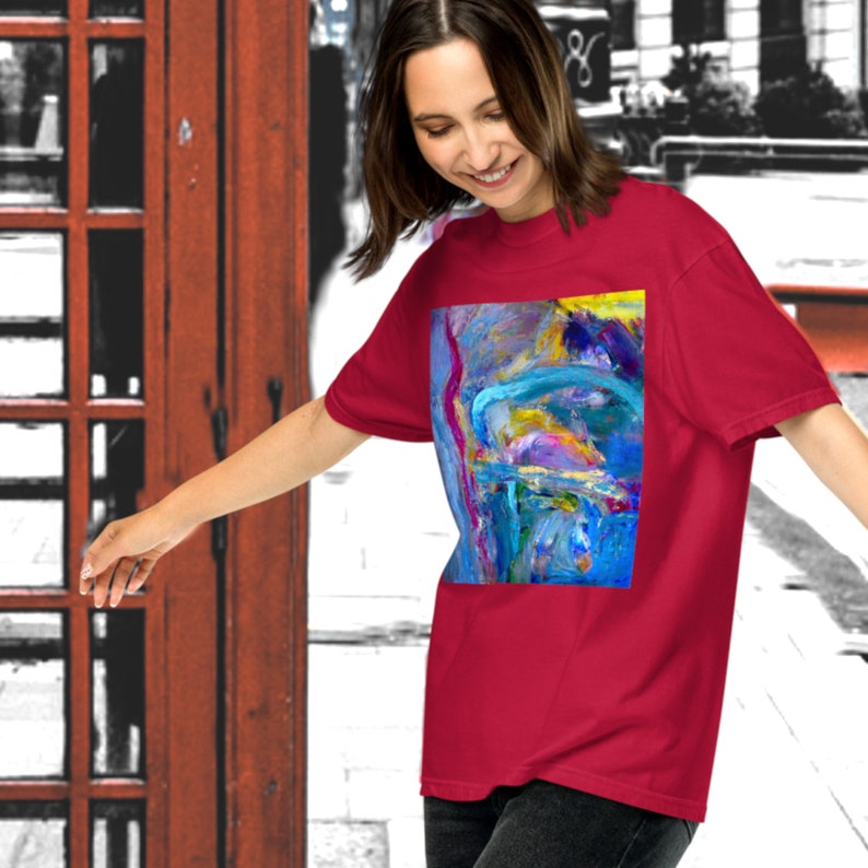 K&ouml;nnte beinhalten: Ein rotes T-Shirt mit einem farbenfrohen abstrakten Malerei-Design. Das Gem&auml;lde zeigt Farbt&ouml;ne von Blau, Gelb, Rosa und Lila.