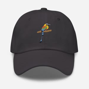 Op de afbeelding: Een donkergrijze baseballcap met een geborduurd vogelontwerp op een tak. De vogel is afgebeeld in levendige kleuren, waaronder geel, blauw en groen. De cap heeft een gebogen klep en een klassiek zes-panelen ontwerp.