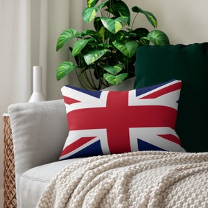 Pode incluir: Uma almofada branca com a bandeira do Reino Unido impressa nela. A almofada está em um sofá branco com uma manta de lã verde.