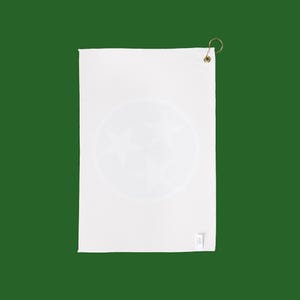 May include: White golf towel with a circular design featuring three stars. The towel has a textured surface and a brass-colored hook for hanging. A small tag is attached to the bottom right corner.