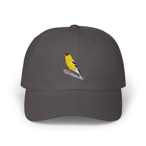Könnte beinhalten: Eine dunkelgraue Baseballkappe mit einem gestickten gelben und schwarzen Vogel auf der Vorderseite.