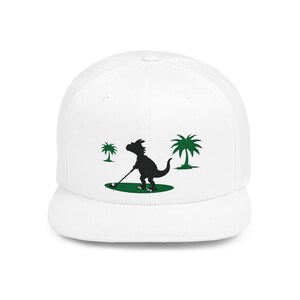 May include: White baseball cap featuring a black silhouette of a dinosaur playing golf on a green golf course with palm trees.