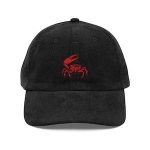 May include: Black corduroy baseball cap with a red embroidered crab design on the front. The cap has a curved brim and an adjustable strap at the back. A casual accessory for everyday wear.
