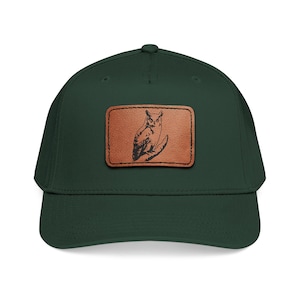 Op de afbeelding: Een donkergroene baseballpet met een gebogen klep. Een rechthoekige bruine leren patch op de voorkant toont een gedetailleerde illustratie van een uil. De pet heeft een klassiek, gestructureerd ontwerp.