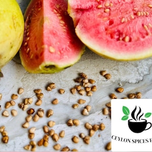 May include: Close-up of guava fruit, cut in half, revealing the pink flesh and seeds. The fruit is on a light gray surface with scattered brown seeds.