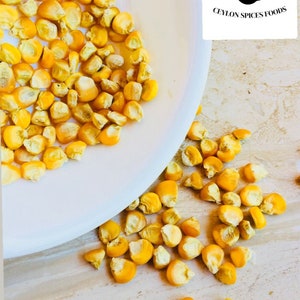 May include: A white bowl filled with bright yellow corn kernels, with some kernels scattered on a light-coloured surface. The Ceylon Spices Foods logo is visible in the upper right corner.