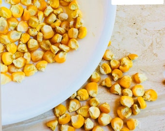 May include: A white plate filled with yellow corn kernels, with more kernels scattered on a light brown surface. The plate is tilted, with some kernels spilling out. The text "CEYLON SPICES FOODS" is visible in the top right corner of the image.