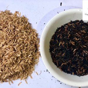 May include: Two piles of rice husks, one pile is light brown and the other is dark brown and black. The dark brown and black pile is in a white bowl. The text "Ceylon Spices Foods" is visible in the top right corner of the image.