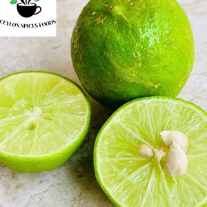 Puede incluir: Tres limas verdes, una entera y dos mitades, se muestran sobre una superficie clara. Las limas cortadas revelan el interior jugoso y las semillas. La imagen incluye el texto "CEYLON SPICES FOODS" con un logotipo de una taza y hojas.