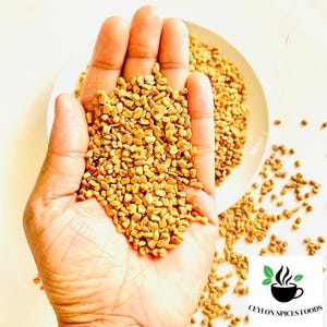 Puede incluir: Una mano sosteniendo un mont&oacute;n de semillas de alholva de color marr&oacute;n dorado, con m&aacute;s semillas derram&aacute;ndose sobre una superficie blanca. Un plato blanco lleno de semillas est&aacute; en el fondo. El logotipo de Ceylon Spices Foods est&aacute; en la esquina inferior derecha.