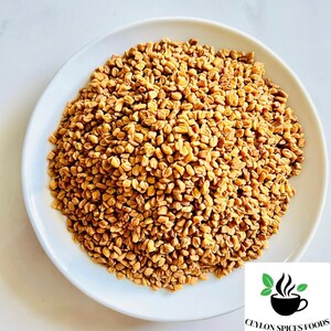 Puede incluir: Un plato blanco rebosante de semillas de alholva de color marr&oacute;n dorado. Las semillas son peque&ntilde;as, de forma irregular y densamente empaquetadas. El logotipo de Ceylon Spices Foods est&aacute; en la esquina inferior derecha.