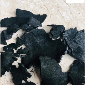 Puede incluir: Primer plano de un mont&oacute;n de trozos de carb&oacute;n vegetal negro sobre una superficie beige claro.