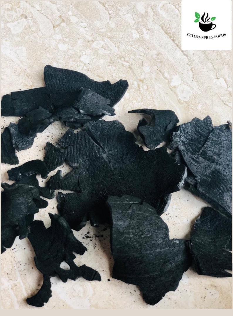 Puede incluir: Primer plano de un mont&oacute;n de trozos de carb&oacute;n vegetal negro sobre una superficie beige claro.