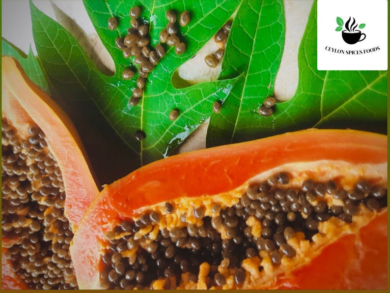 Op de afbeelding: Een close-up van een doormidden gesneden papaya, die het oranje vruchtvlees en de zwarte zaden laat zien. De papaya ligt op een groen blad met een witte achtergrond.