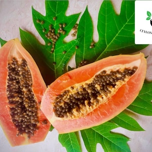 May include: Two halves of a ripe papaya with black seeds are displayed on a green papaya leaf. The papaya is a tropical fruit with a sweet and juicy flavour.