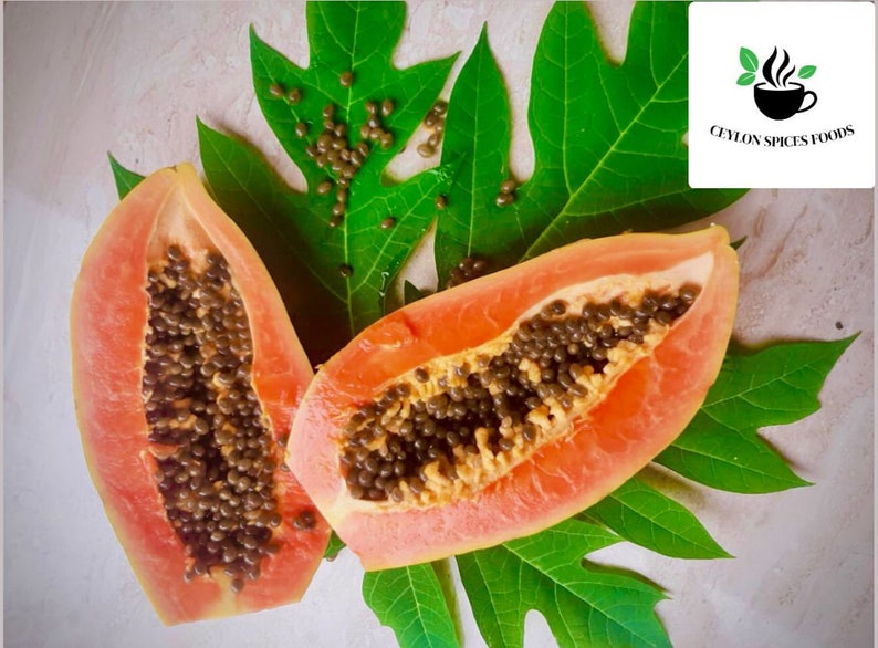 Op de afbeelding: Twee helften van een rijpe papaja met zwarte zaden worden getoond op een groen papajablad. De papaja is een tropisch fruit met een zoete en sappige smaak.