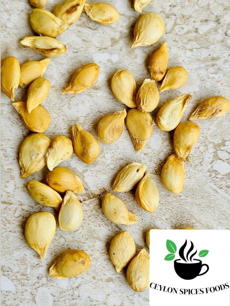May include: A close-up of a pile of dried apricot kernels. The kernels are a pale yellow color and have a slightly wrinkled texture.