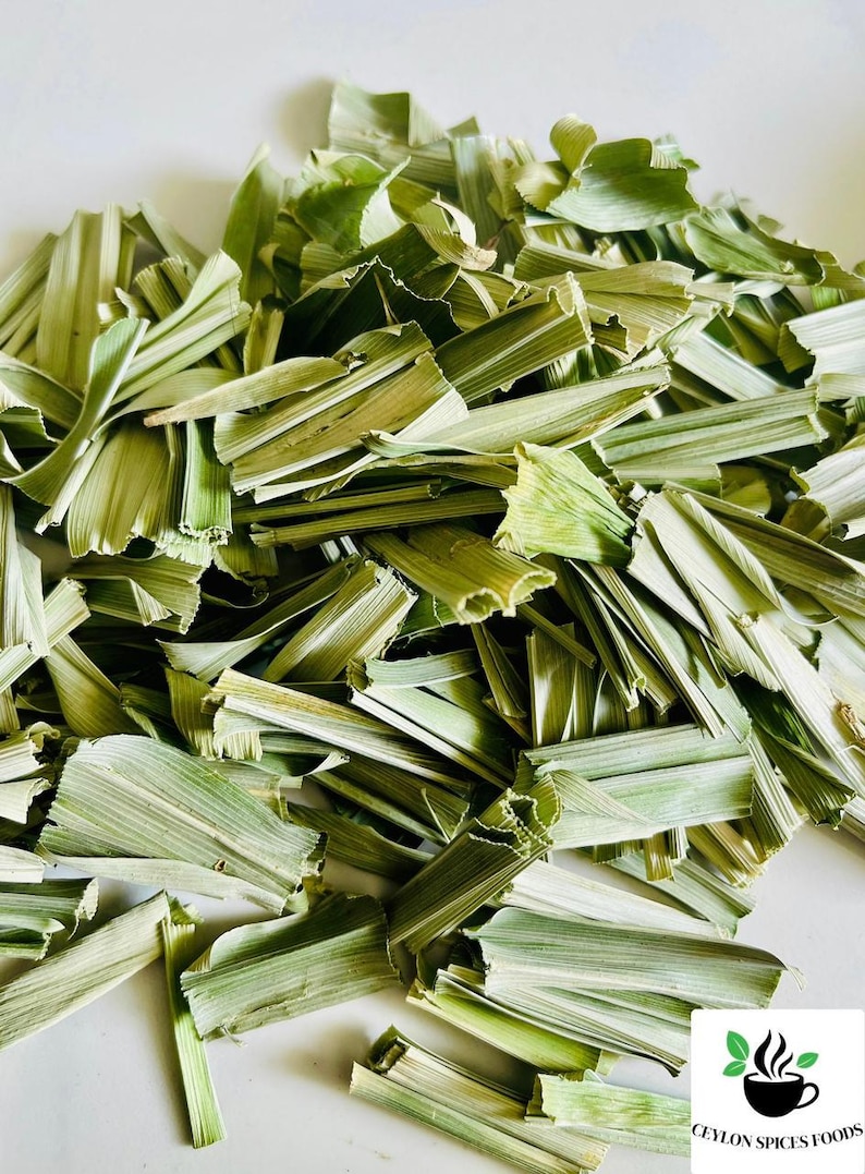 May include: A pile of dried, light green lemongrass stalks cut into small, uniform segments. The pieces are fibrous and have a pale, muted color. In the bottom right corner, a logo features a black coffee cup icon with green leaves.