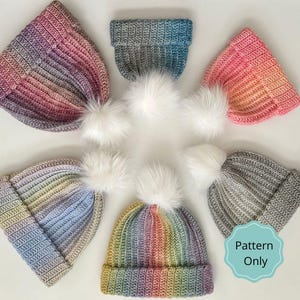 Può includere: Una collezione di berretti lavorati a maglia a coste fatti a mano in vari colori, tra cui arcobaleno, rosa e grigio, ciascuno sormontato da un soffice pompon bianco. I berretti sono disposti a cerchio. Il testo "Pattern Only" è visibile.