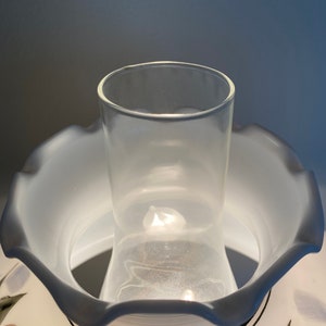 May include: A white ceramic lampshade with a scalloped edge and a floral design. The lampshade has a clear glass chimney inside.
